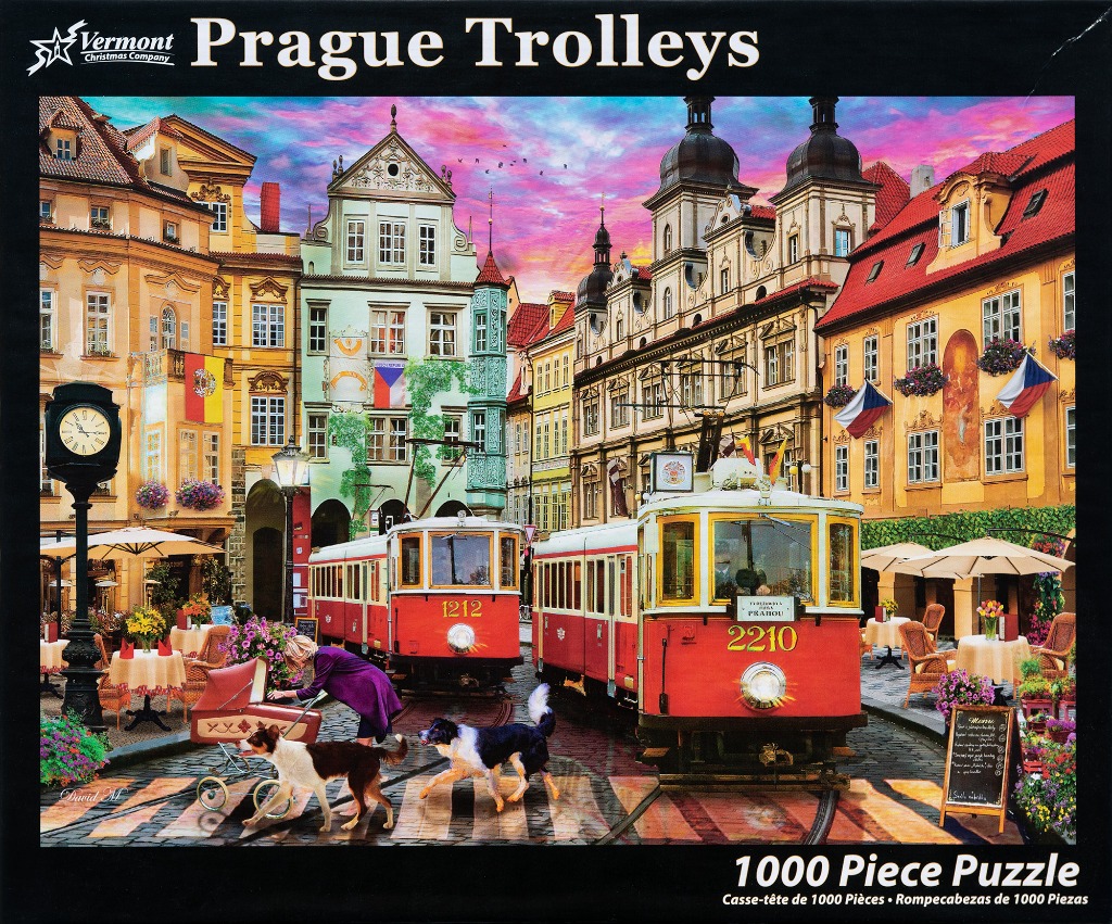 A street scene in Prague featuring two vintage red and yellow electric trams, historic buildings, and a sunset sky.