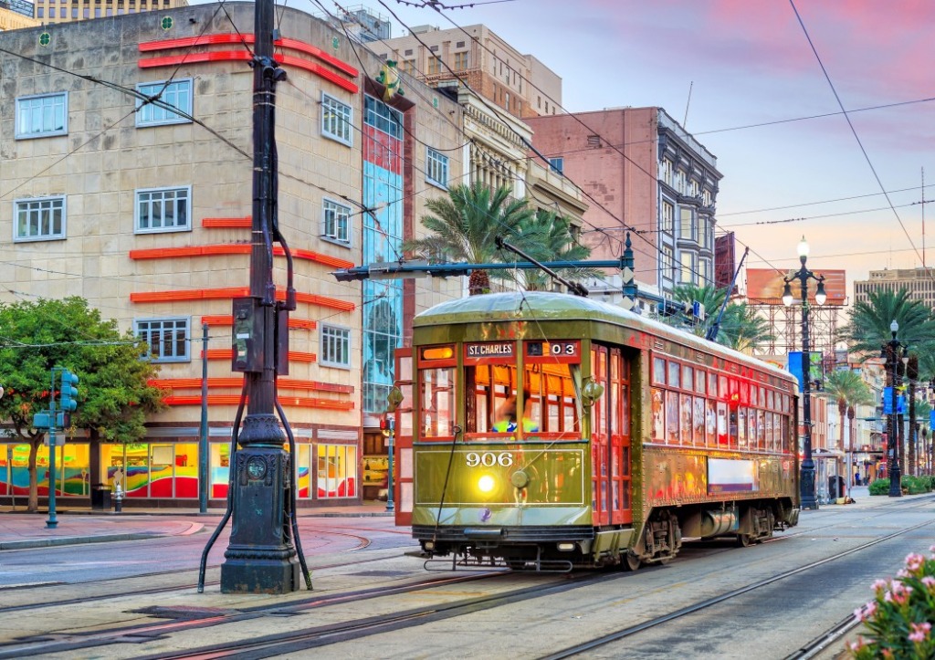 A vintage green and red streetcar traveling along city tracks past an Art Deco building at twilight.