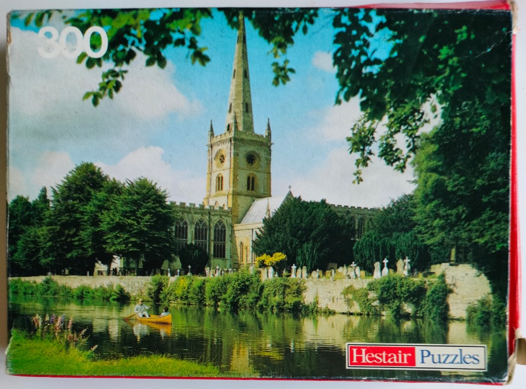 A peaceful canal scene featuring a historic stone church with a tall spire, framed by trees and greenery.