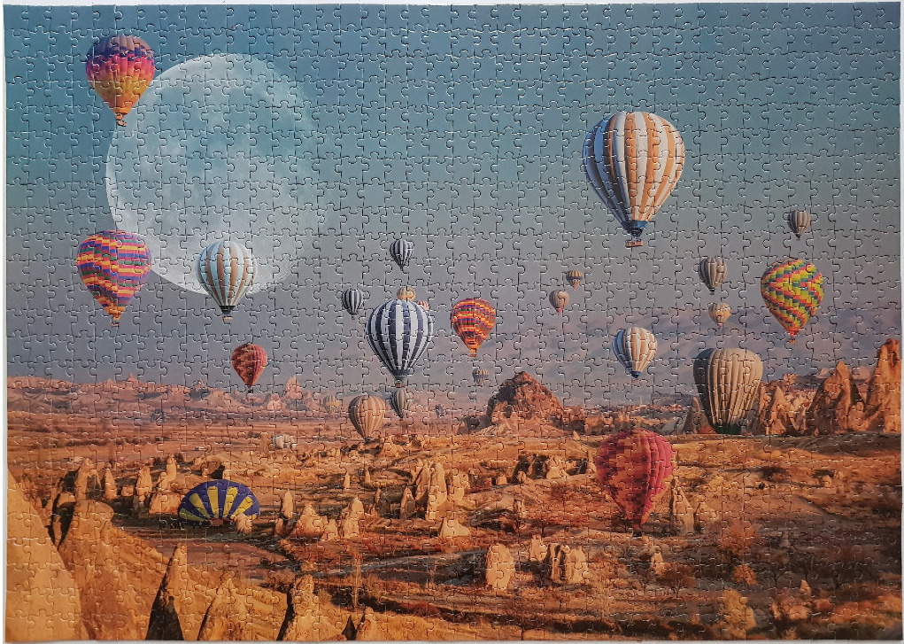 Many hot air balloons floating over a rugged desert landscape with a large moon in the sky.