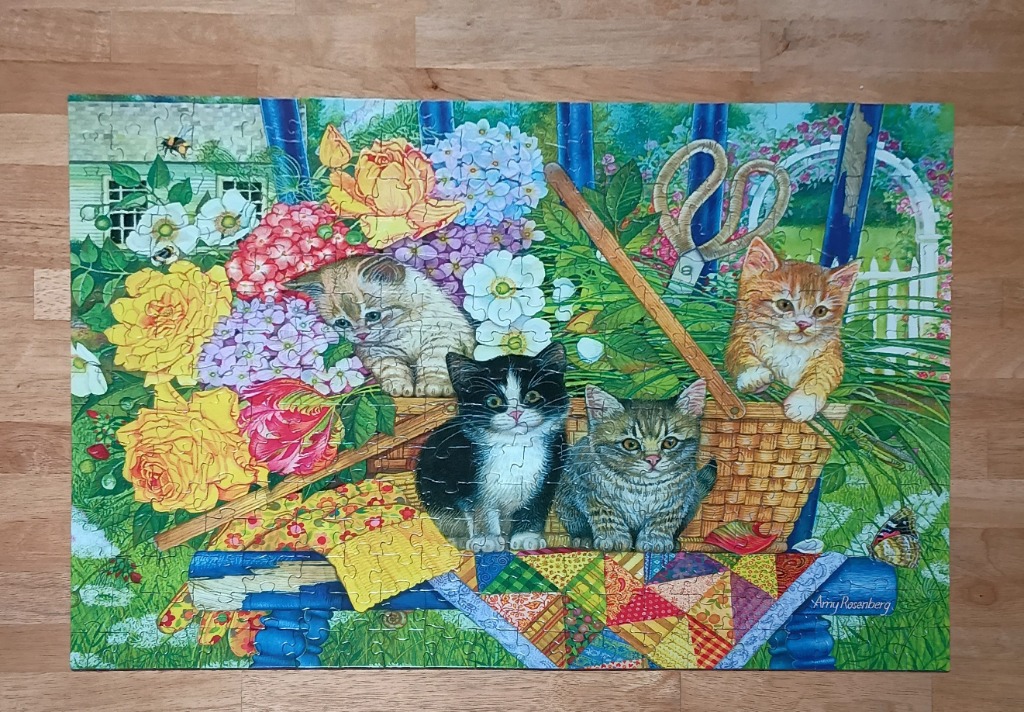 Four kittens sitting in and around a wicker basket in a lush, floral garden setting.