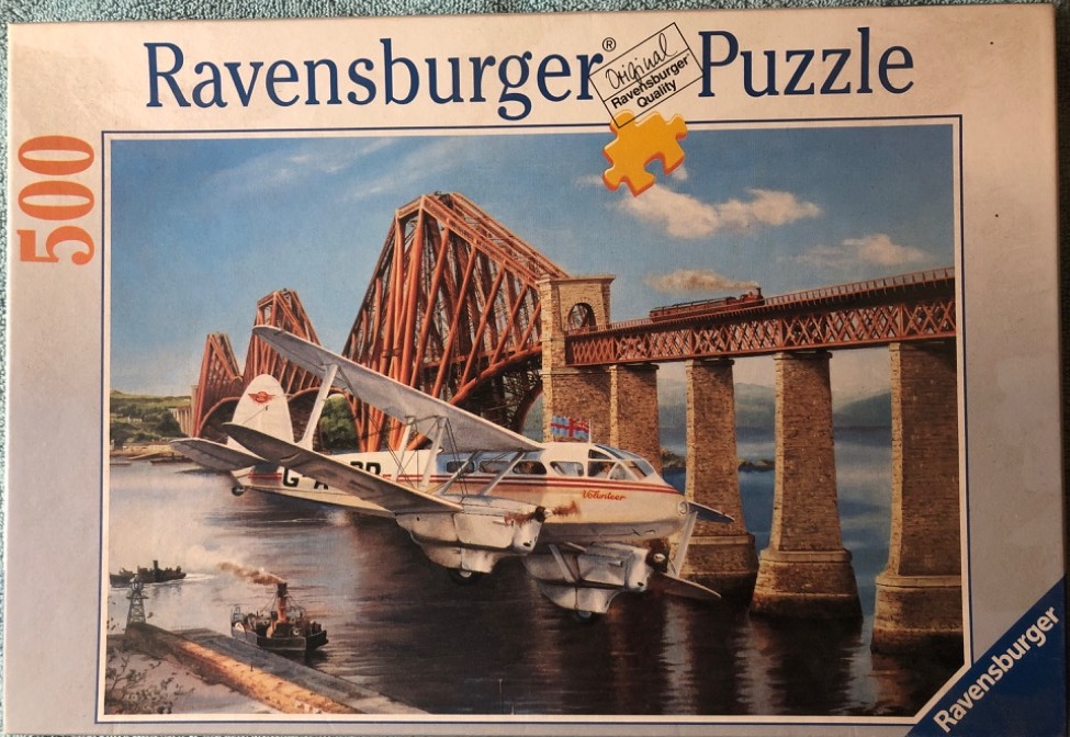 A vintage aircraft flying over the water in front of the Forth Bridge in Scotland.