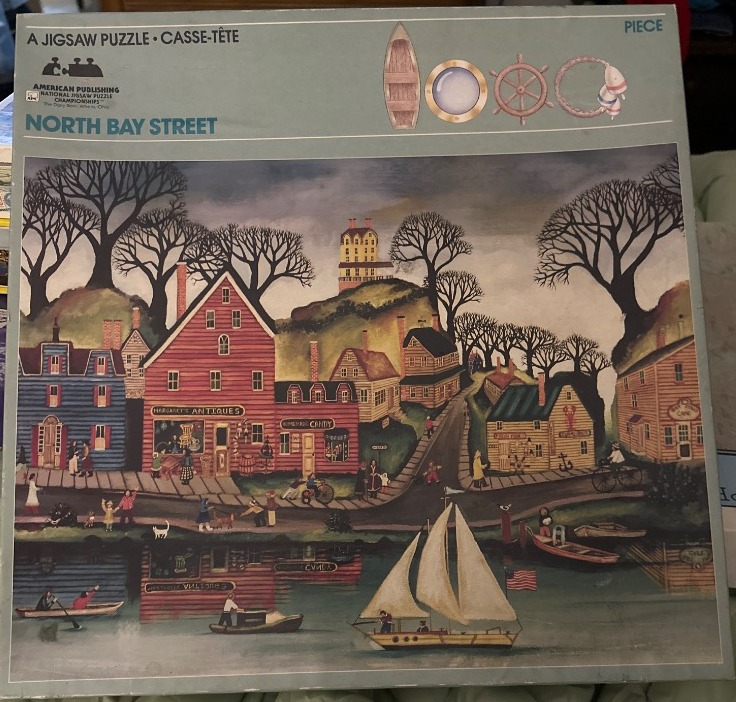A folk art painting of a coastal town street with shops, a harbor, a sailboat, and leafless trees under a grey sky.