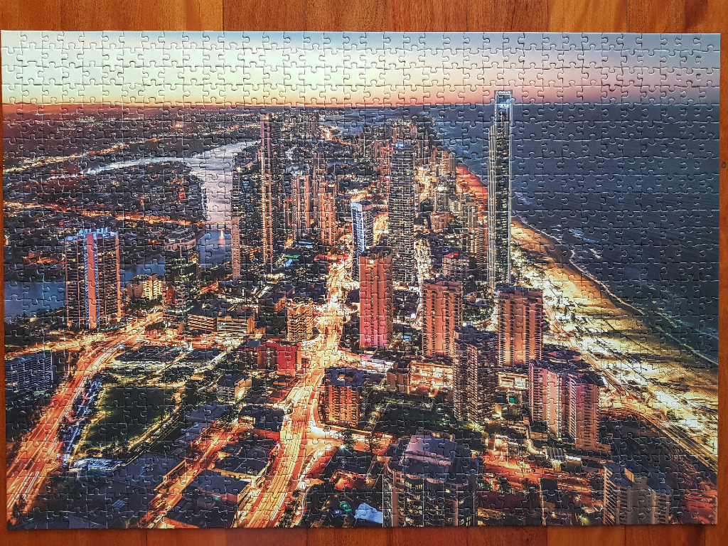 Aerial view of a coastal city at twilight with glowing skyscrapers and city lights.