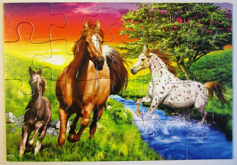 Three horses running through a grassy meadow by a stream at sunset