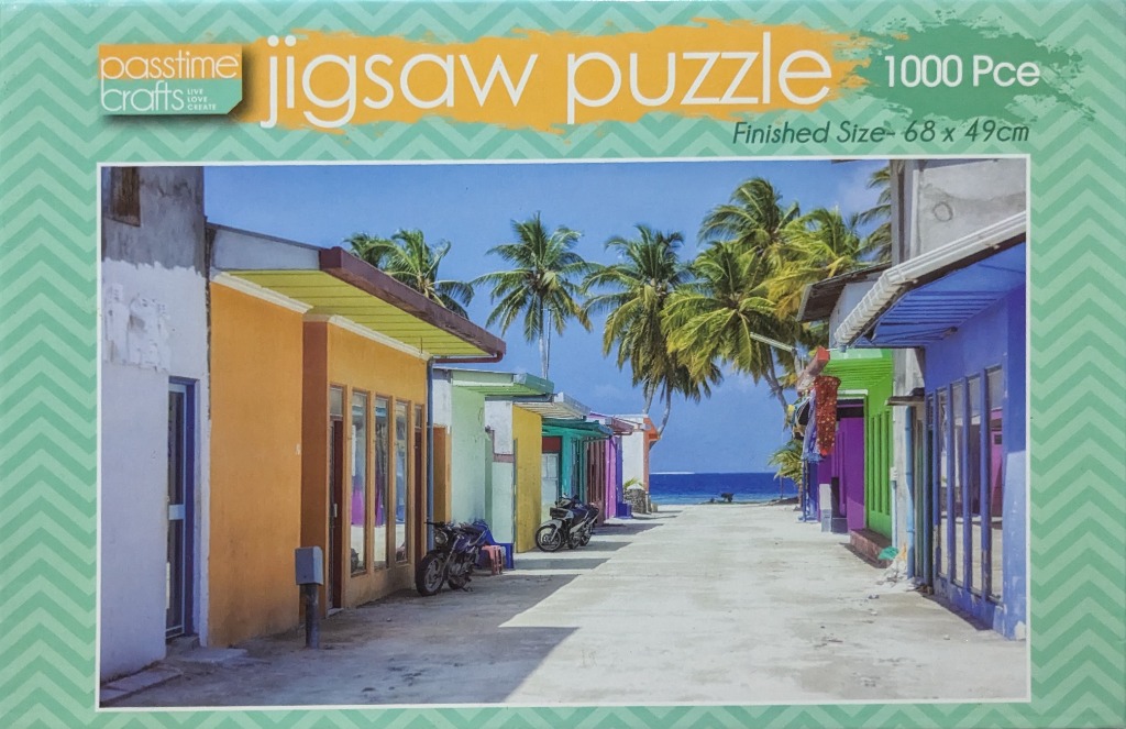 A sunny tropical street scene with colorful buildings leading toward a turquoise ocean and palm trees.