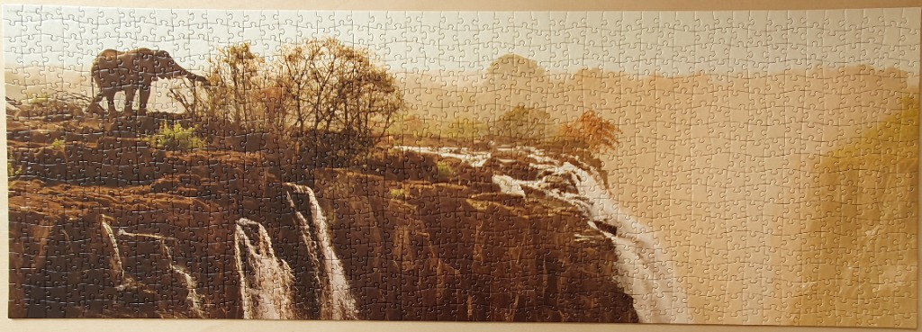 A panoramic landscape featuring a lone elephant standing on a rocky precipice above a waterfall in hazy golden light.