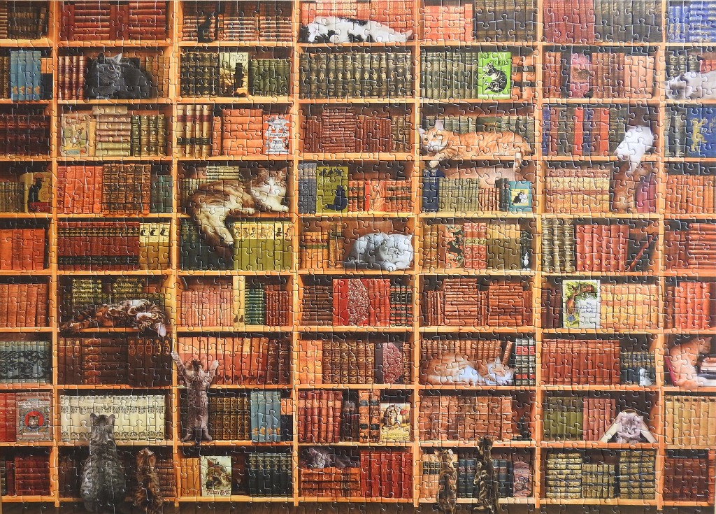 A library bookcase filled with many books and cats resting on the shelves.