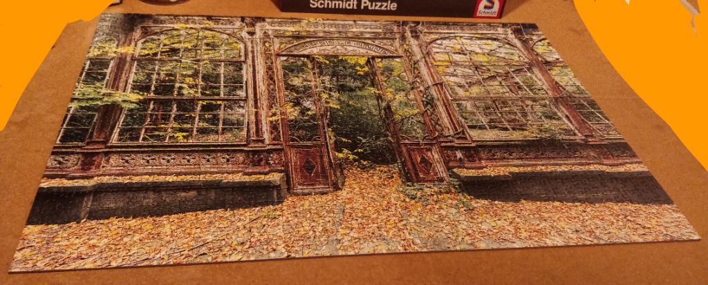 An abandoned greenhouse structure in autumn surrounded by fallen leaves and lush foliage.