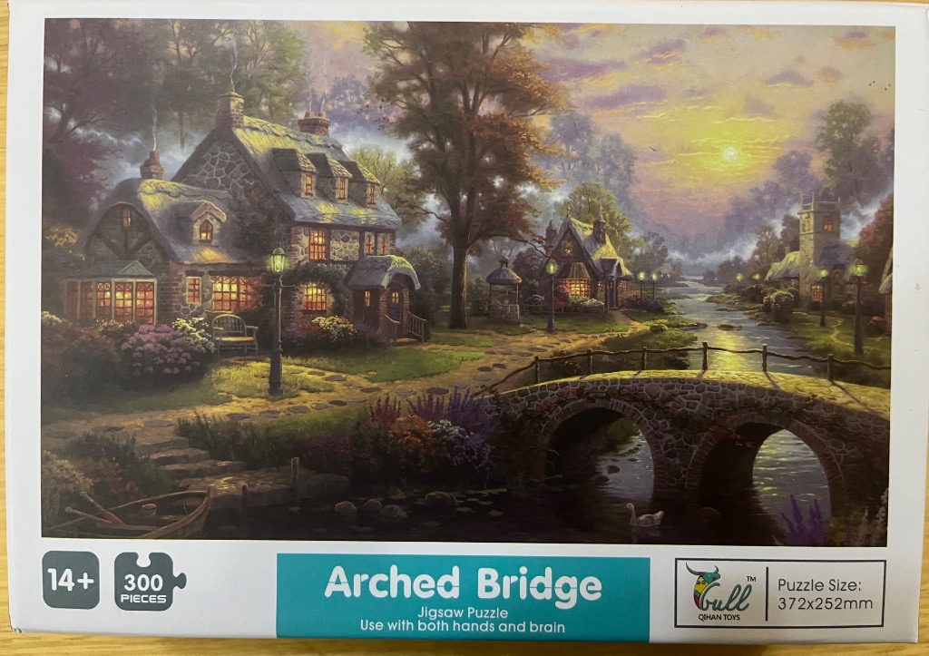 A peaceful English countryside scene at sunset featuring a stone cottage, an arched bridge, and a winding river.