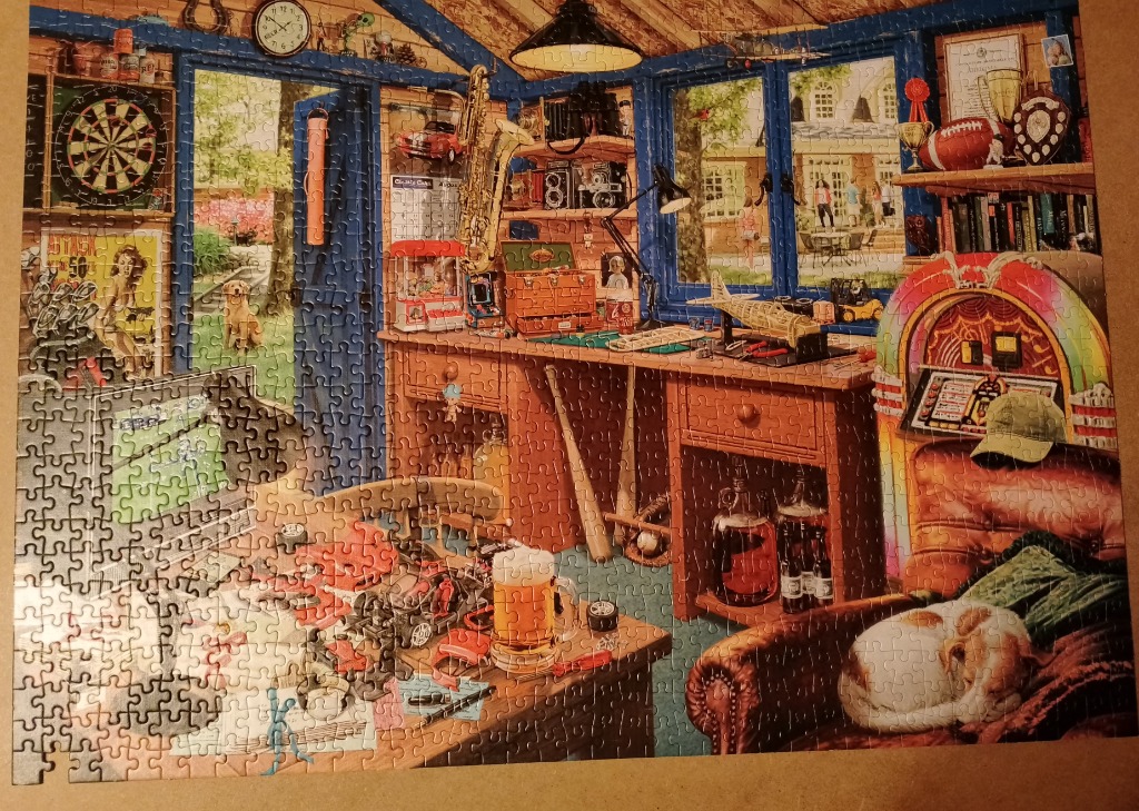 A cluttered, cozy hobby workshop filled with vintage items, a jukebox, and a golden retriever outside.