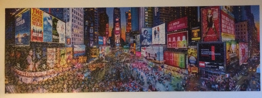 A panoramic view of Times Square in New York City at twilight, filled with bright billboards and a crowd of people.