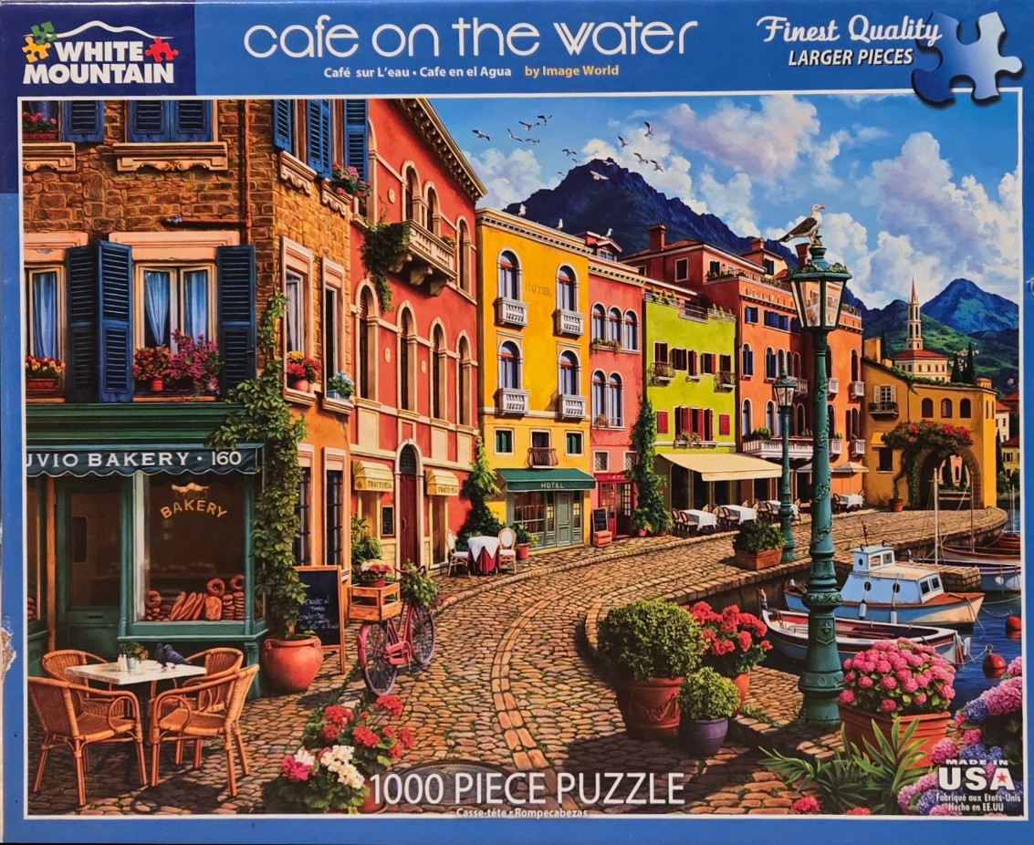A colorful painting of a cobblestone cafe street along a waterfront, flanked by vibrant historic buildings.