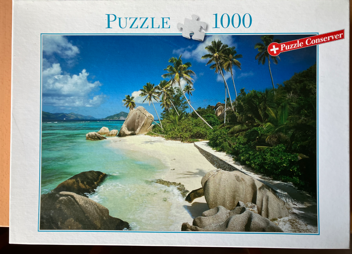 A tropical beach scene with white sand, turquoise water, large granite boulders, and leaning palm trees under a blue sky.