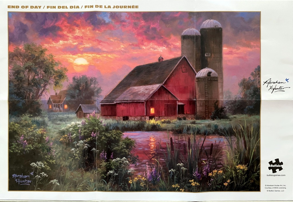 A red barn and silos beside a tranquil pond at sunset.
