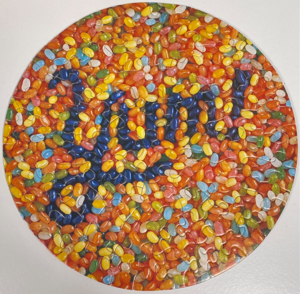 A circular image filled with a dense pile of colourful jelly beans, with some beans arranged to spell the word LOVE.