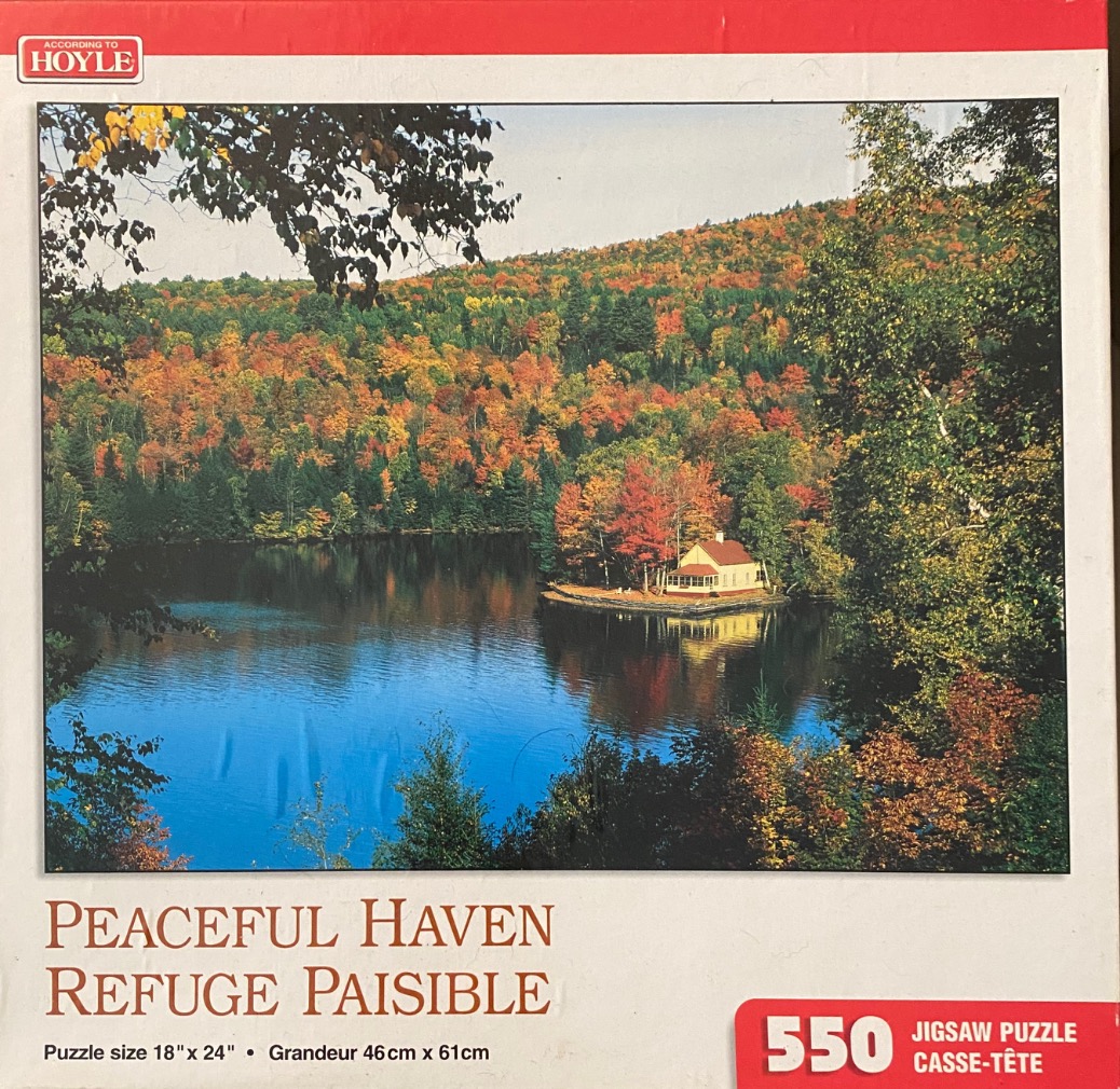 A photograph of a small house on a wooded lake shore during autumn, surrounded by vibrant fall foliage.