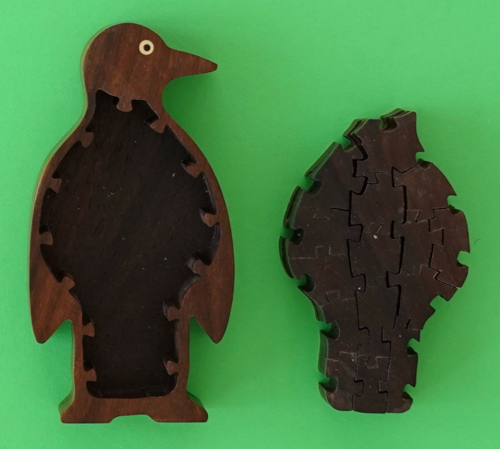 A hollow wooden penguin frame next to an assembled dark wood penguin-shaped object against a flat green background.