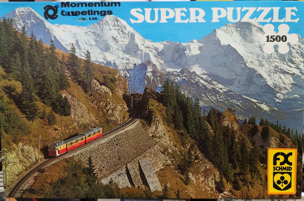 A red and yellow train traversing a mountainous landscape with snow-capped peaks in the background.