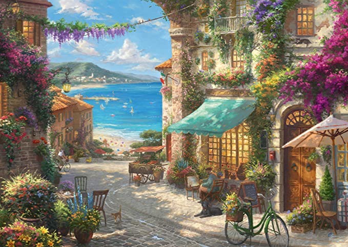 A sunny Mediterranean seaside village street with cobblestones, flowering bougainvillea, a cafe, and ocean views.