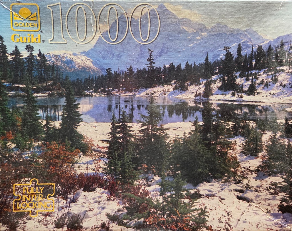 A scenic winter mountain landscape with a still lake surrounded by snow-covered pine trees.