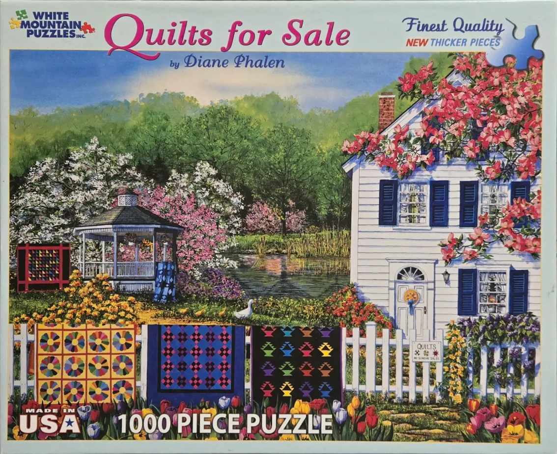 A peaceful country scene featuring a white house, a gazebo by a pond, and colorful quilts hanging on a picket fence.