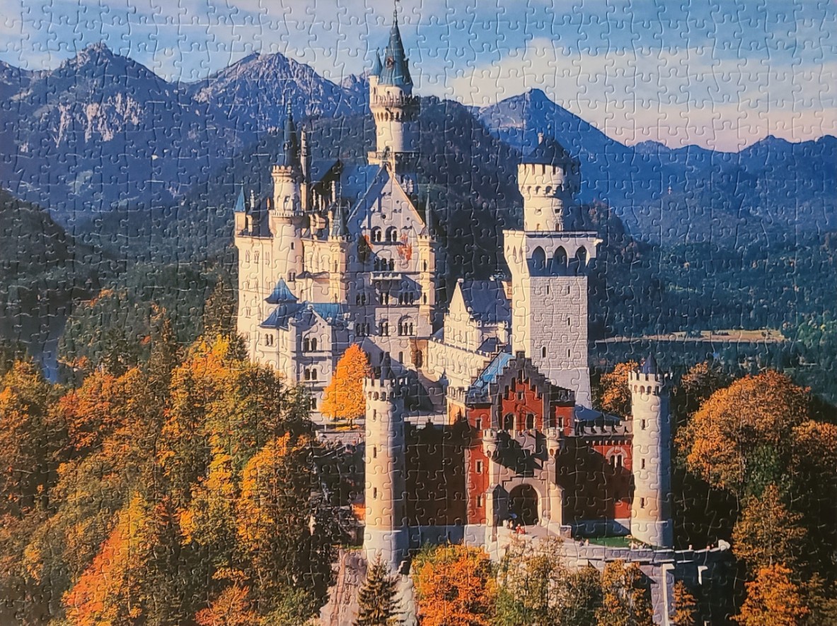 Neuschwanstein Castle nestled in a vibrant autumn forest with mountains in the background.