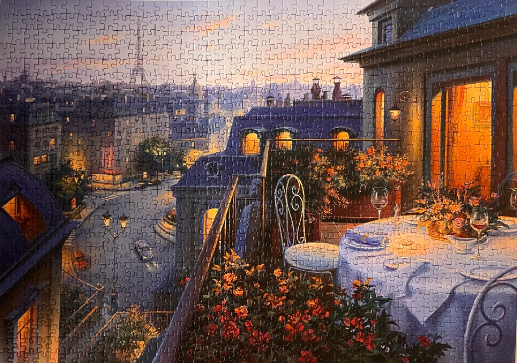 An outdoor balcony dining scene overlooking a Parisian street at sunset with the Eiffel Tower in the distance.