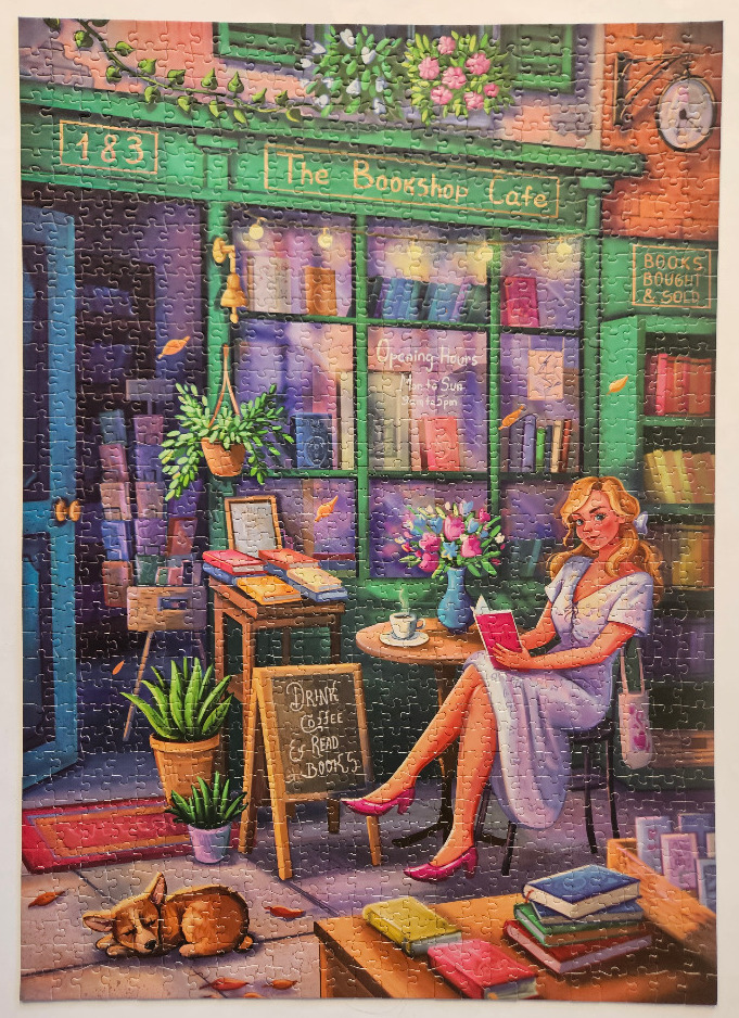 A woman reading a book outside a charming green-fronted bookshop cafe with a sleeping dog.