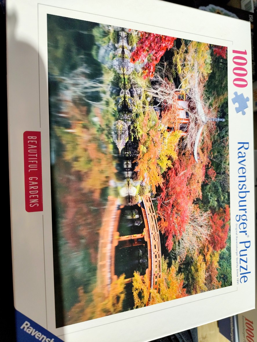 A scenic Japanese garden with a red bridge and pagoda reflected in a pond during autumn.