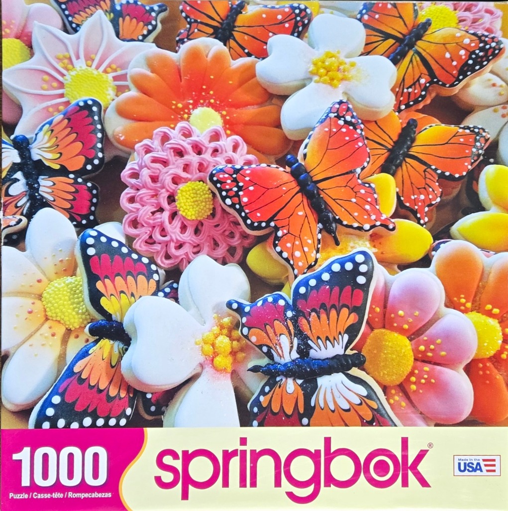 A close-up view of numerous cookies shaped like bright flowers and monarch butterflies, layered together.