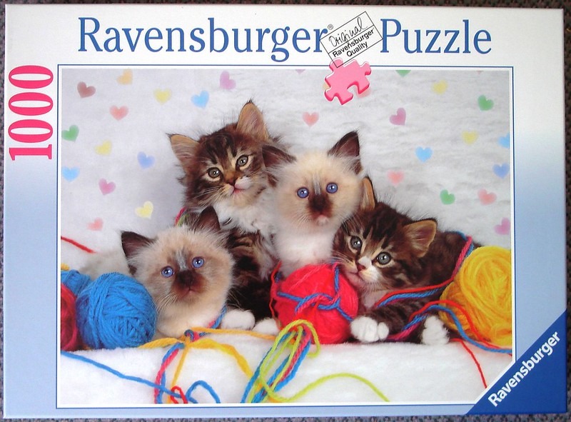 Four fluffy kittens sitting among colorful balls of yarn against a heart-patterned background.