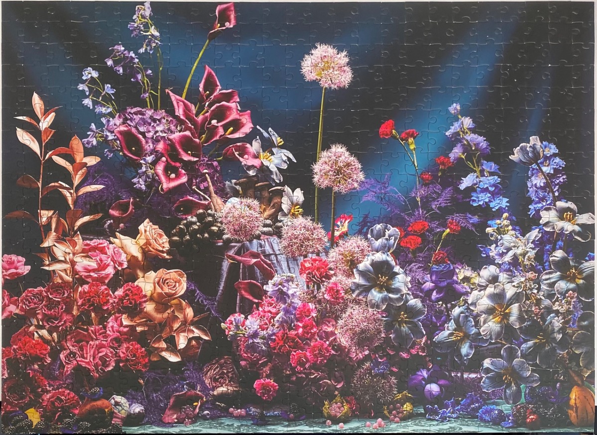 A lush, dark-toned floral still life arrangement in shades of deep purple, pink, and blue.