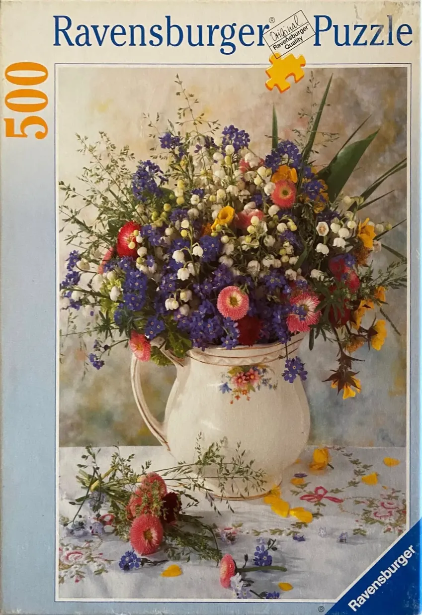 A lush bouquet of wildflowers in a white ceramic pitcher sits on a tablecloth.