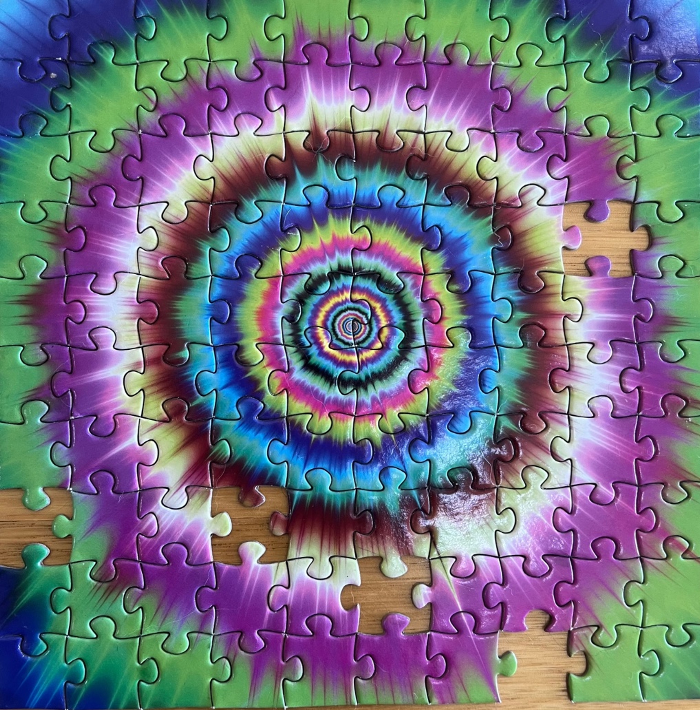A psychedelic tie-dye style circular fractal pattern with vibrant purple, blue, green, and pink colors.