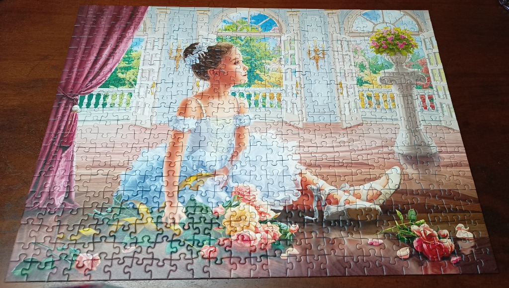 A young girl in a white dress sits on a wooden floor in a grand room filled with flowers.