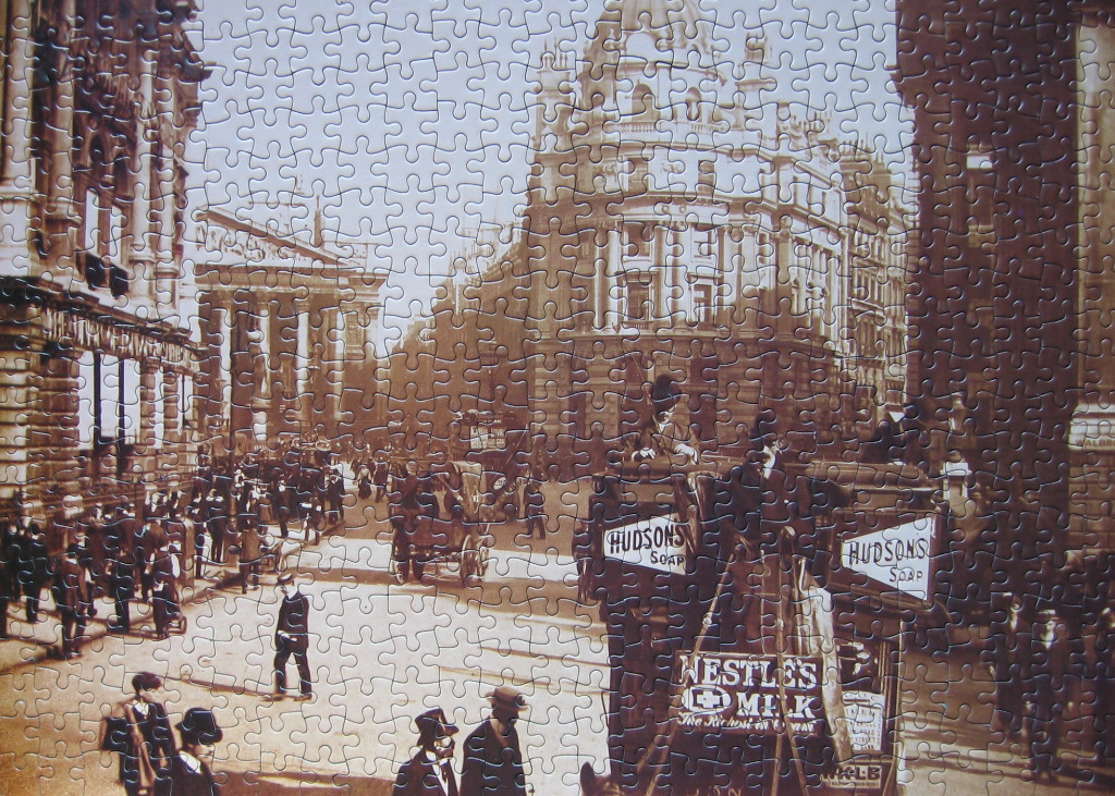 A sepia-toned historical street scene showing a bustling 19th-century city square with ornate architecture and carriages.