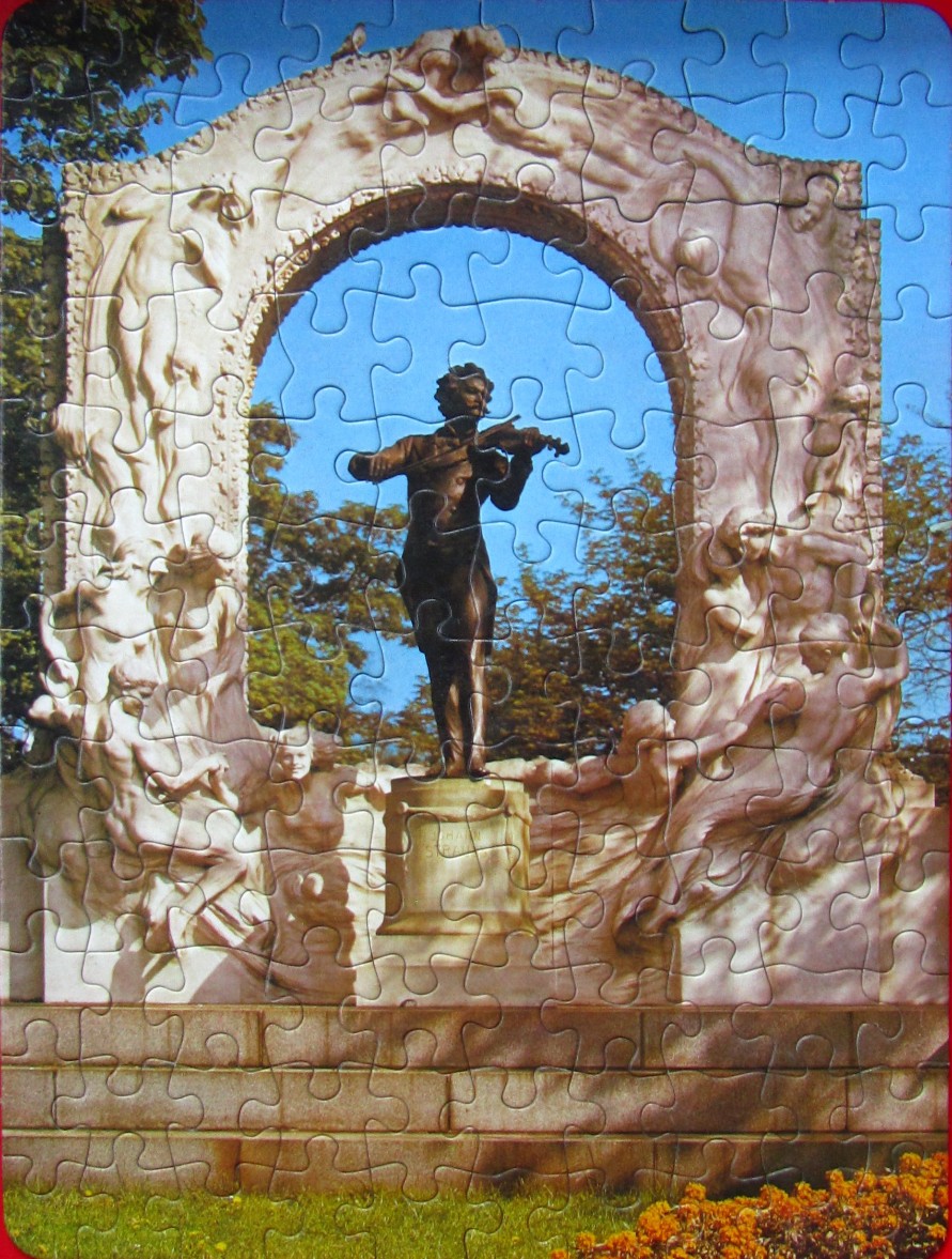 The Johann Strauss II monument in Vienna featuring a bronze statue of the violinist under a white marble arch.