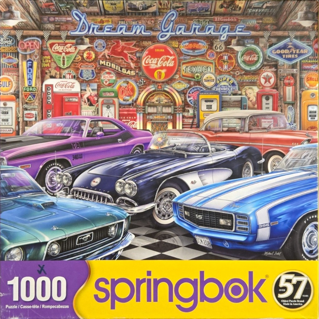 A collection of classic American muscle cars parked in front of a nostalgic garage wall covered in vintage metal signs.
