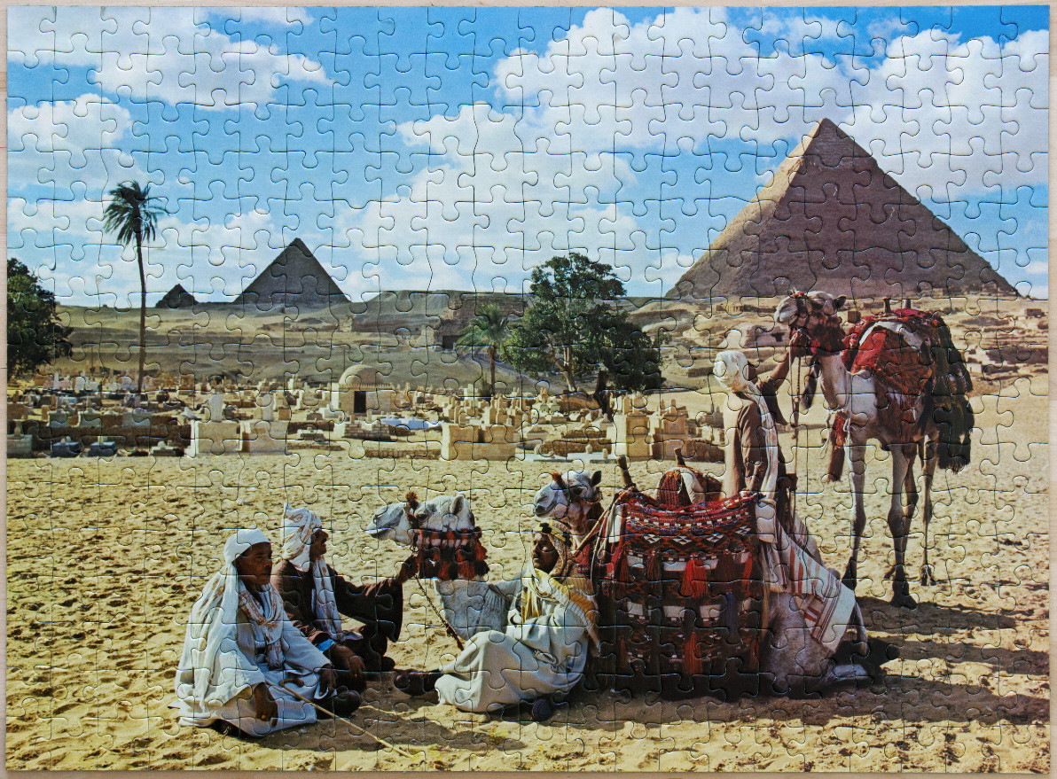 Three men in traditional clothing resting with camels in front of the Giza pyramids.