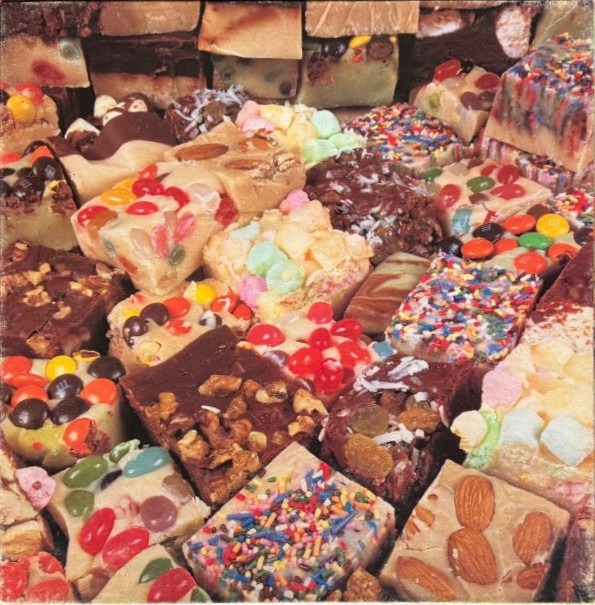 A close-up, top-down view of a dense collection of square-cut pieces of fudge, topped with various candies and nuts.