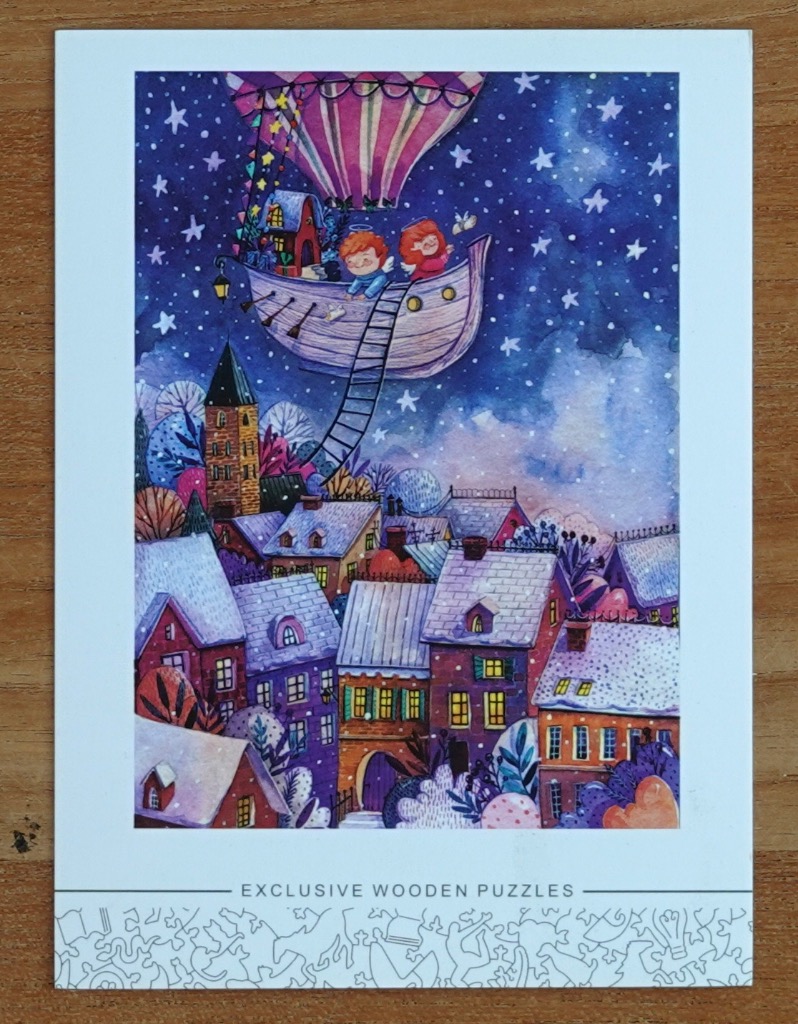 Two angels in a boat carried by a hot air balloon floating above a snowy village at night.