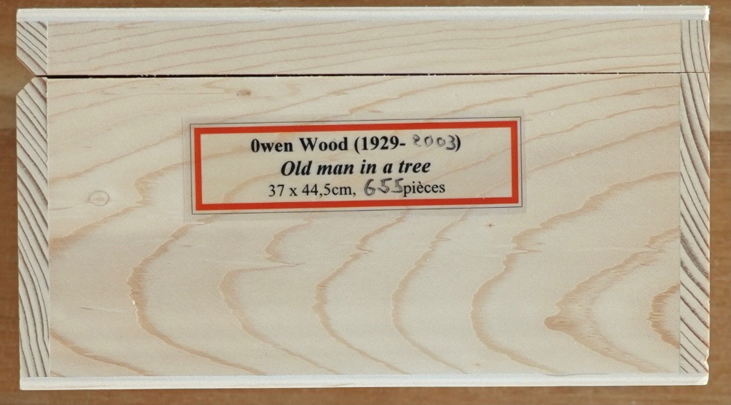 A rectangular light wood box with a central paper label detailing the artist, title, dimensions, and piece count.