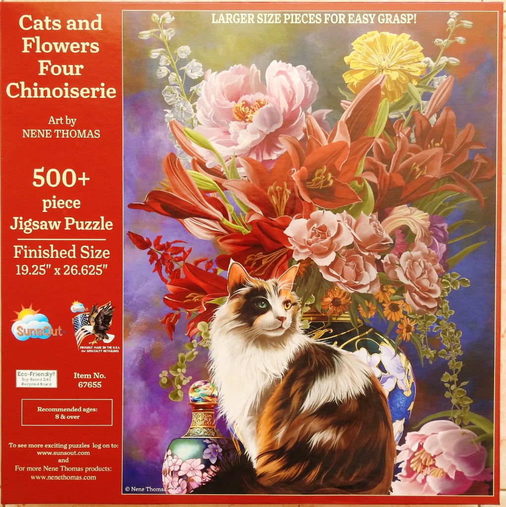 A long-haired tortoiseshell cat sits in front of a vibrant floral arrangement in a dark vase.