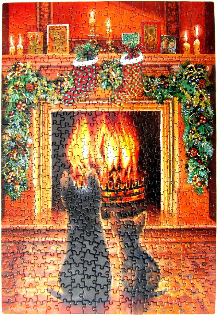 Two black cats sitting in front of a cozy fireplace decorated for Christmas.