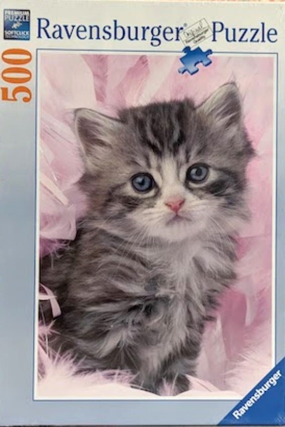 A close-up photograph of a fluffy, grey and white tabby kitten sitting among soft pink feathers.