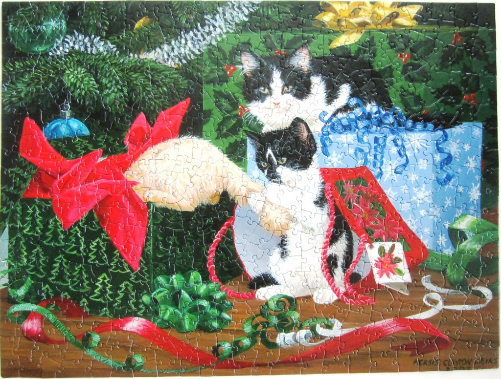 Two black and white kittens playing with Christmas gifts and ribbons under a tree.