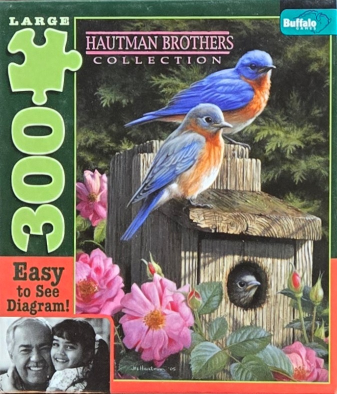 Two eastern bluebirds perched on a wooden birdhouse with pink flowers in the foreground.