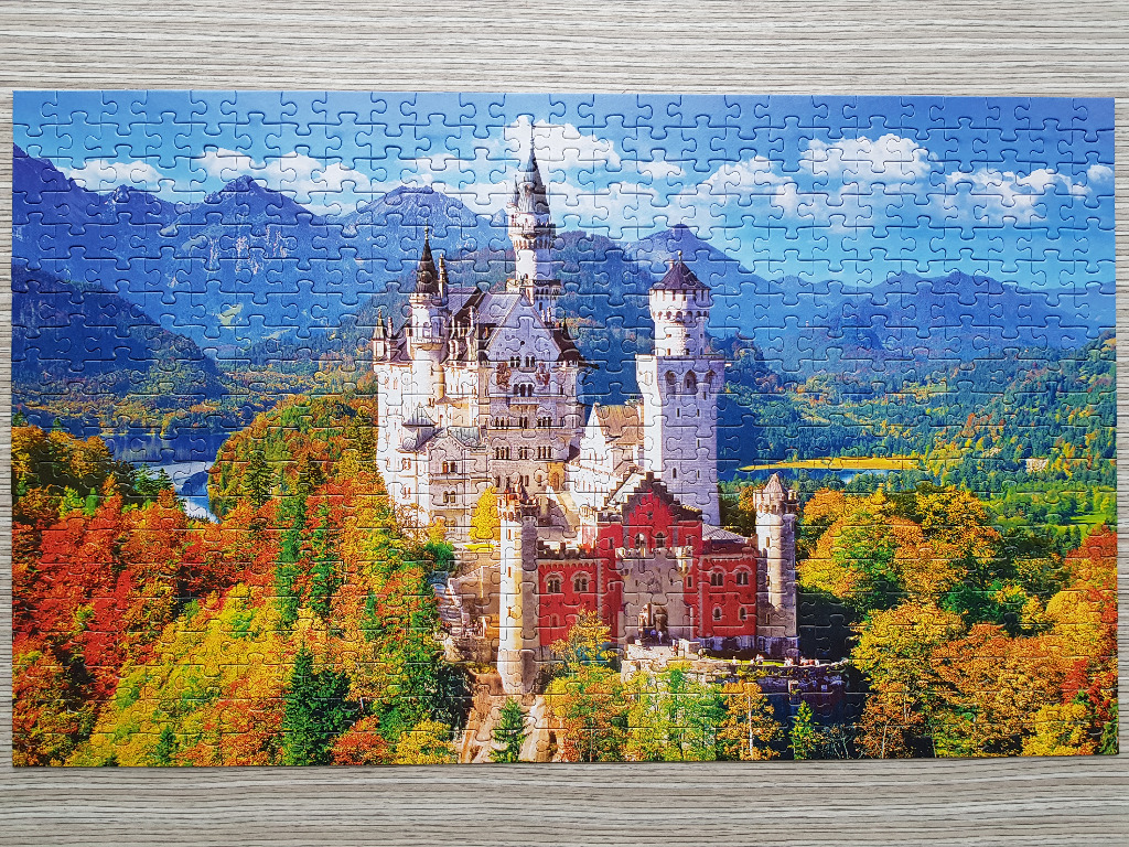 A panoramic view of Neuschwanstein Castle surrounded by autumn foliage and mountains under a blue sky.