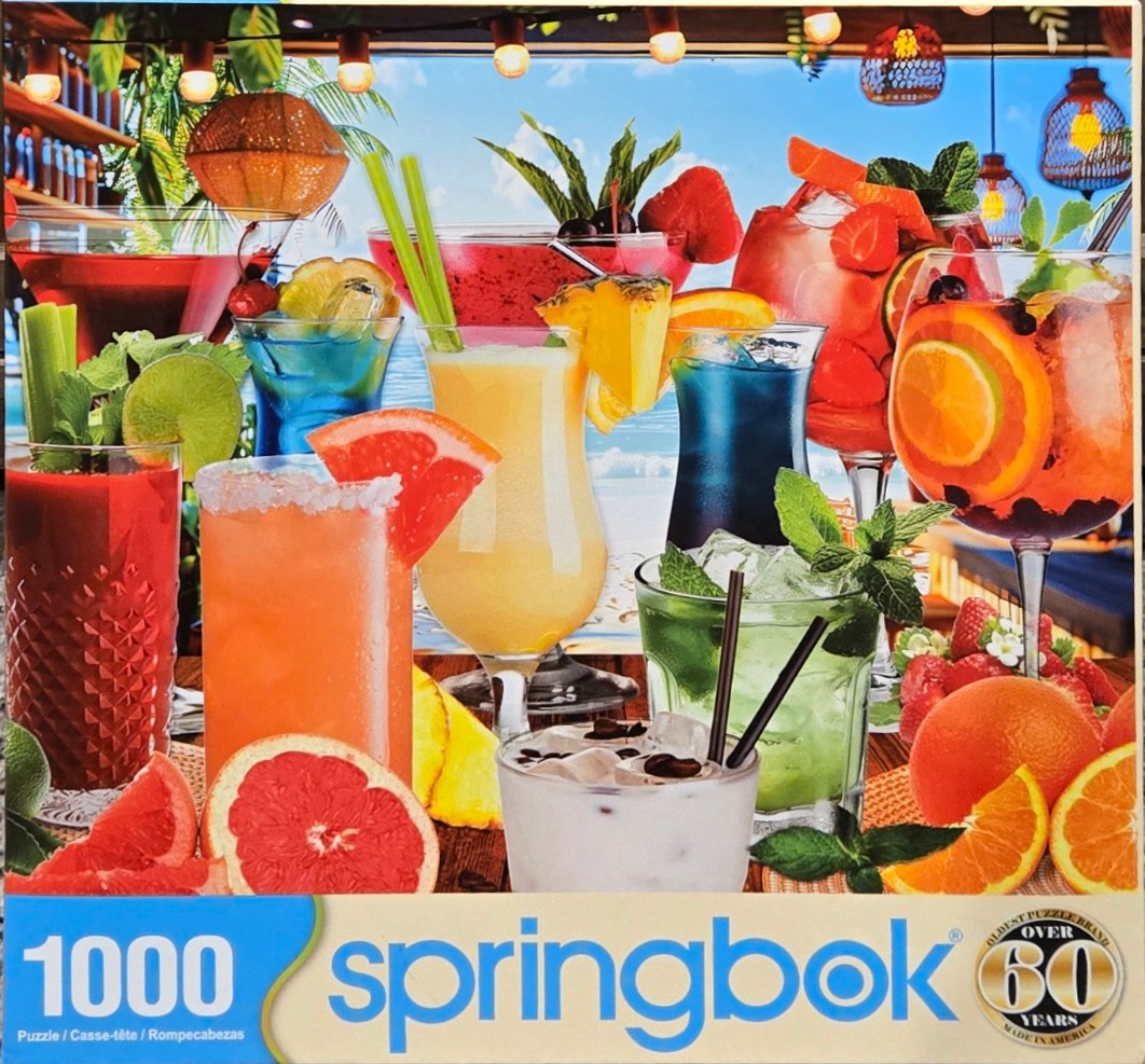 A collection of colorful tropical cocktails and fresh fruit arranged on a wooden surface by the ocean.
